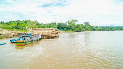 Fototapeta premium Timber loaded into big barge then drag by a tugboat cruising Mahakam River, Borneo, Indonesia