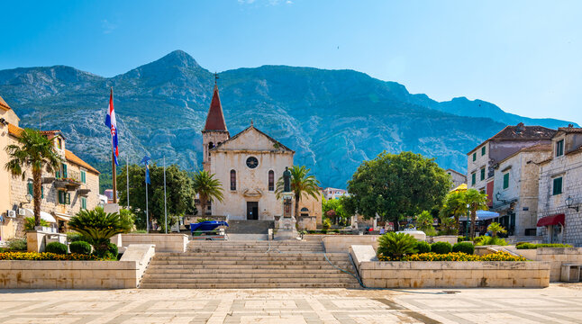 Saint Marko cathedral and church at Makarska city, Croatia. The Biokovo mountains in the background. Sunny day at summer, green trees on the side. Dalmatia region.