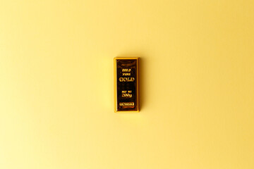 A gold bar on a yellow background. Financial concept. Flat lay. Top view. The concept of a gold reserve. A protective financial asset. The stock market. Golden ETF