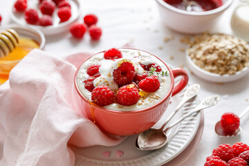 Porridge with the addition of fresh raspberries, yogurt and honey served in a pink cup, close-up view. A healthy breakfast or dessert
