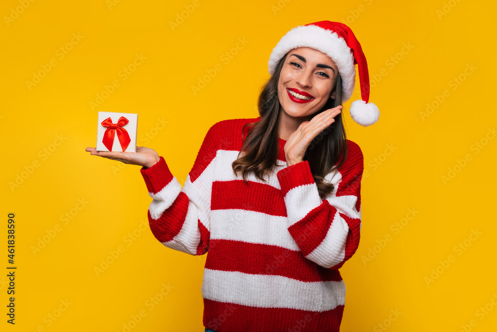 Wall mural cute excited smiling woman with christmas gift box in hands is having fun while posing on yellow bac