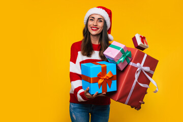 Close up photo of beautiful excited smiling woman with many cool Christmas gift boxes in hands while she is having fun and posing on yellow background