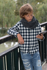 10-year-old blond boy with light eyes, Caucasian, looking and enjoying with his mobile in his hand, autumn clothes and torn jeans