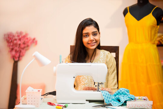 Portrait of Young indian woman tailor or fashion designer using sewing machine at tailoring workshop