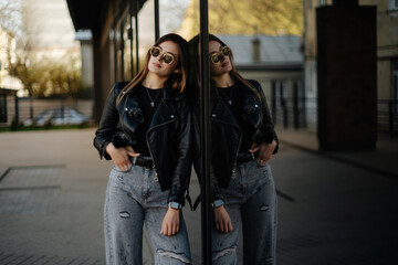 Young woman wearing black t-shirt, glasses and leather jacket posing against street