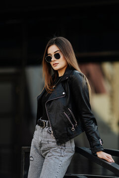 Young woman in sunglasses and black leather jacket posing outdoor