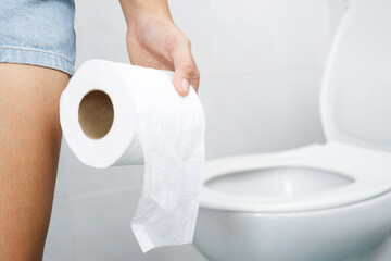 portrait of a woman suffers from diarrhea his stomach painful. ache and problem. hand hold tissue paper roll in front of toilet bowl. constipation in bathroom. Hygiene, health care concept.