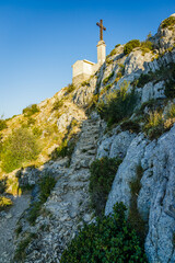 Fototapeta premium View of the Croix de Provence cross, and the top of Montagne Sainte-Victoire mountain from the northern rocky trail of the Sainte-Victoire Priory in Provence, France