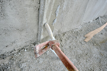Trowel and adze in front of the recently made plastered wall by concrete. Red colors exist on handle of the adze made of wooden material. after construction works.