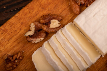 Sliced camembert and walnut kernels on a wooden cutting board, close-up, selective focus.
