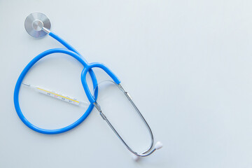 The blue stethoscope lies on a white background with a thermometer in the middle. . High quality photo