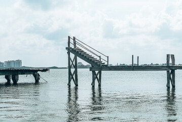 Abandoned and damaged wooden jetty bridge with staircase over sea water surface against cloudy sky
