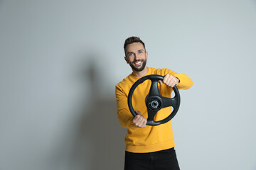 Happy man with steering wheel on grey background