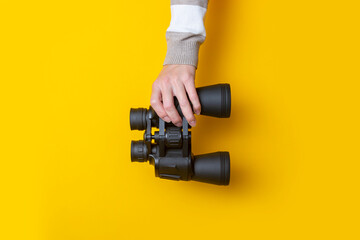 Fototapeta na wymiar Woman's hand holds binoculars on a bright yellow background