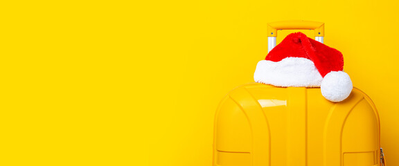 Santa Claus hat lies on top of a yellow suitcase on a yellow background. Banner