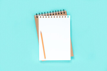 Notebook with pencil. School notebook on light blue background, spiral notepad on table. Top view of open notebook with blank pages, office notepad flat lay. White Page for your write. Copy Space
