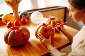 Close up of woman hands with knife carving pumpkin. On the table lies a orange pumpkin with a painted horrible face. Halloween, decoration and holidays concept.