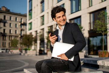 The banker is standing near the business center. A manager in a suit is working on a laptop near the office on the street.