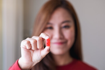 Closeup image of a young woman holding and showing at a red jelly gummy bears