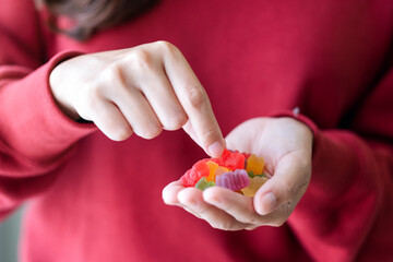 Closeup image of a young woman holding and showing at a red jelly gummy bears