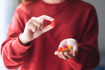 Closeup image of a young woman holding and showing at a red jelly gummy bears