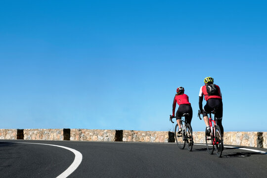 Couple of cyclists with a red T-shirt rides on the streets of Palma de Mallorca, in a sunny day. Spain, Europe.