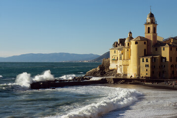 Stunning view of the picturesque town of Camogli with its church on the sea and the waves crashing on the dock.