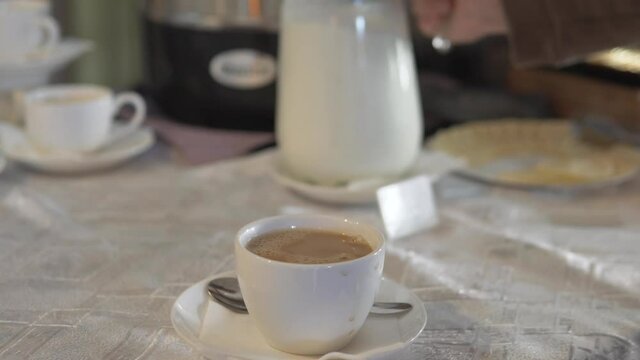 Close-up, milk is added to a porridge with coffee in a restaurant with a buffet system. The visitor adds milk to the coffee.