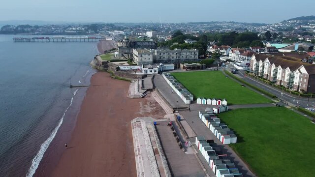 Aerial drone shot flying up on Paington beach, revealing Redcliffe hotel, pier and beach huts in on the coast of Tor Bay in Devon, England