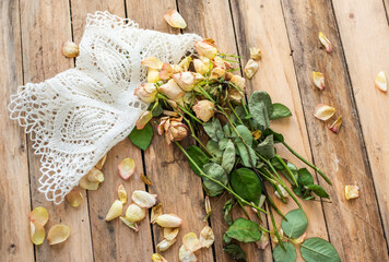 Trockene Rosen auf Untergrund aus Holz mit Spitzendecke – Blüten und Blätter