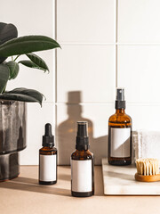Amber bottles with white labels and houseplant in ceramic pot on beige table and wall white tiles.