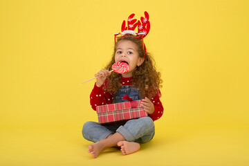 Little girl for the Christmas holidays with a gift and a lollipop on a yellow background to copy  space