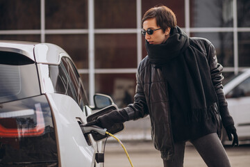 Fototapeta premium Woman charging electro car at the street