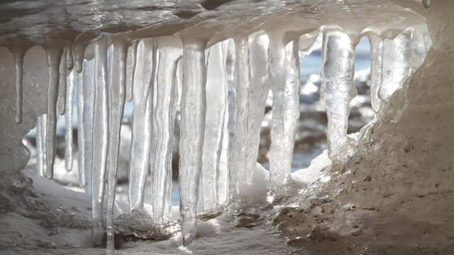 An ice grotto on the seashore. A row of icicles blocked the exit from it. The waves are moving behind them.