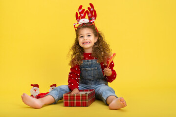 Little girl for the Christmas holidays with a gift and a lollipop on a yellow background to copy  space