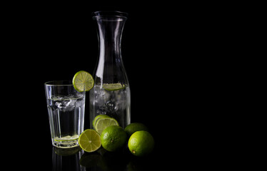 Jug or pitcher and glass of water with lime fruits. Copy space on black background.
