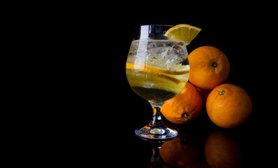 Glass of cold refreshing water, with ice and oranges fruits. Copy space on black background.