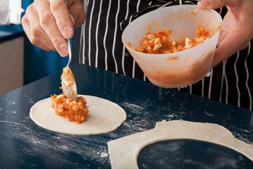 Manos de chef rellenando empanadillas de atún. Chef's hands filling tuna dumplings. - obrazy, fototapety, plakaty