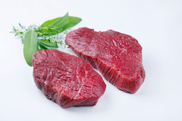 Raw dry aged bison beef rump steak slices with herbs offered as close-up on white background with...