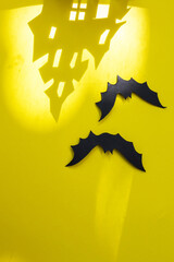 Halloween and decoration concept - bats, pumpkins, gloomy paper house, gloomy black tree branches on a yellow background. house made of paper with a shadow from the house, gloomy shadows of halloween.