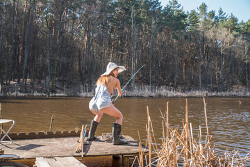 A girl stands on the shore of a forest lake and catches fish with a fishing rod. - Powered by Adobe