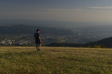 Fototapeta premium man walking up the hill above the city at sunset 