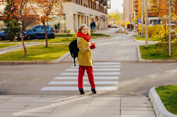 Woman with a cup of coffee about to cross the road on a zebra crossing in the city