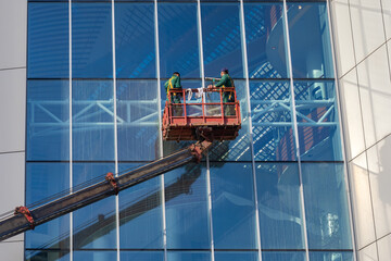 Skyscraper window washers at work. Two people on crane tower are washing glass. Concept - work of...