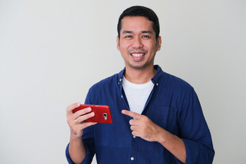 Adult Asian man smiling while pointing finger to his mobile phone