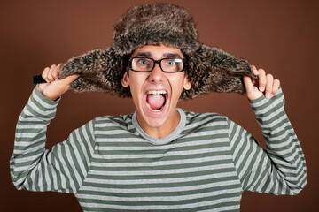 Portrait of a funny and surprised man in a winter hat on a brown background. The guy with the glasses.