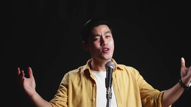 Asian Man Singer Singing Into Microphone On Black Background
