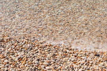 a pebble beach on a sunny day. clear sea water and rocks on the seashore or ocean. copy space. natural trend background 2022. stone texture