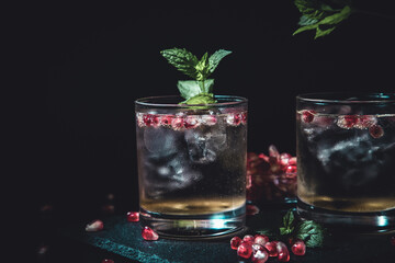 two moody cocktails on a black background with mint and pomegranate