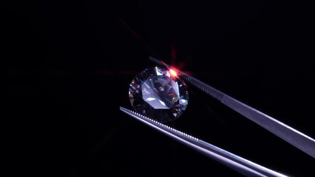 Diamond in tweezers selective focus, inspection and analyzing of brilliant cut crystal polish quality. Jewellery professional hand making in the studio. Macro shot, shallow depth of view.